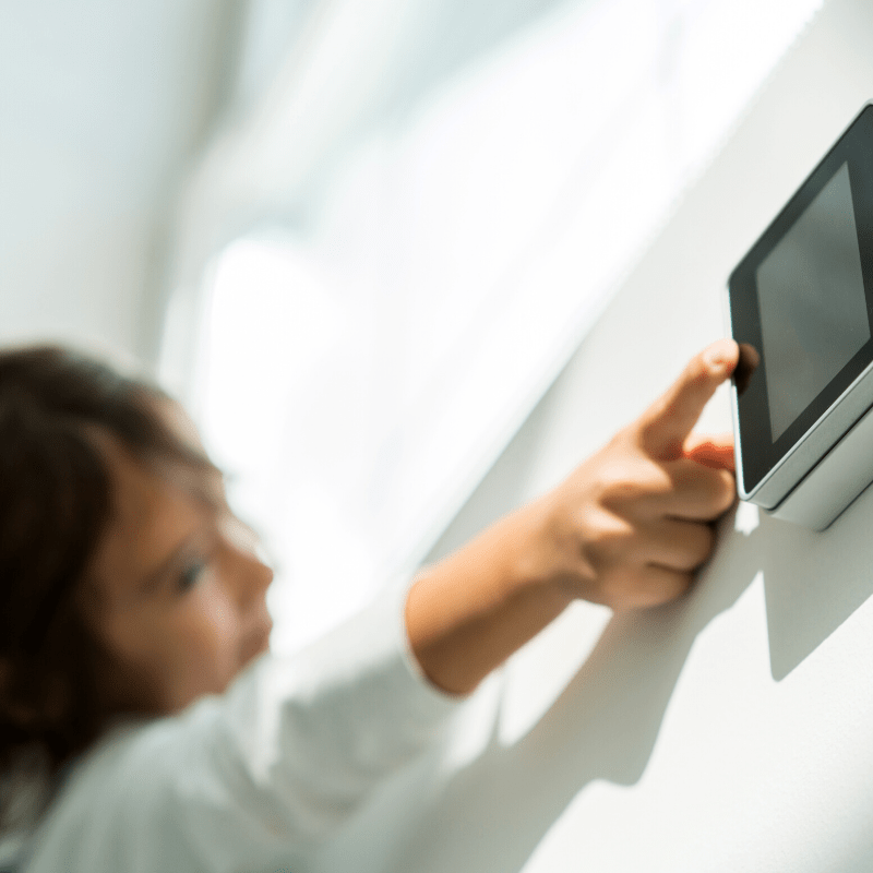 Young child reaching to touch a smart home device on the wall in her home